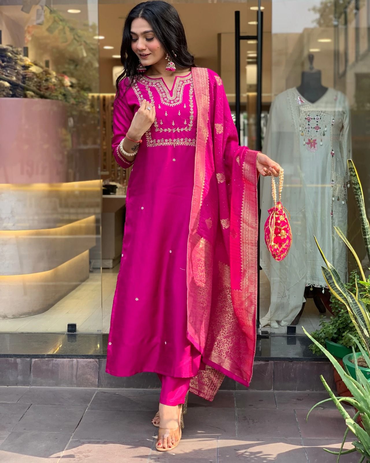 Woman in a bright pink traditional outfit standing in front of a store with mannequins.