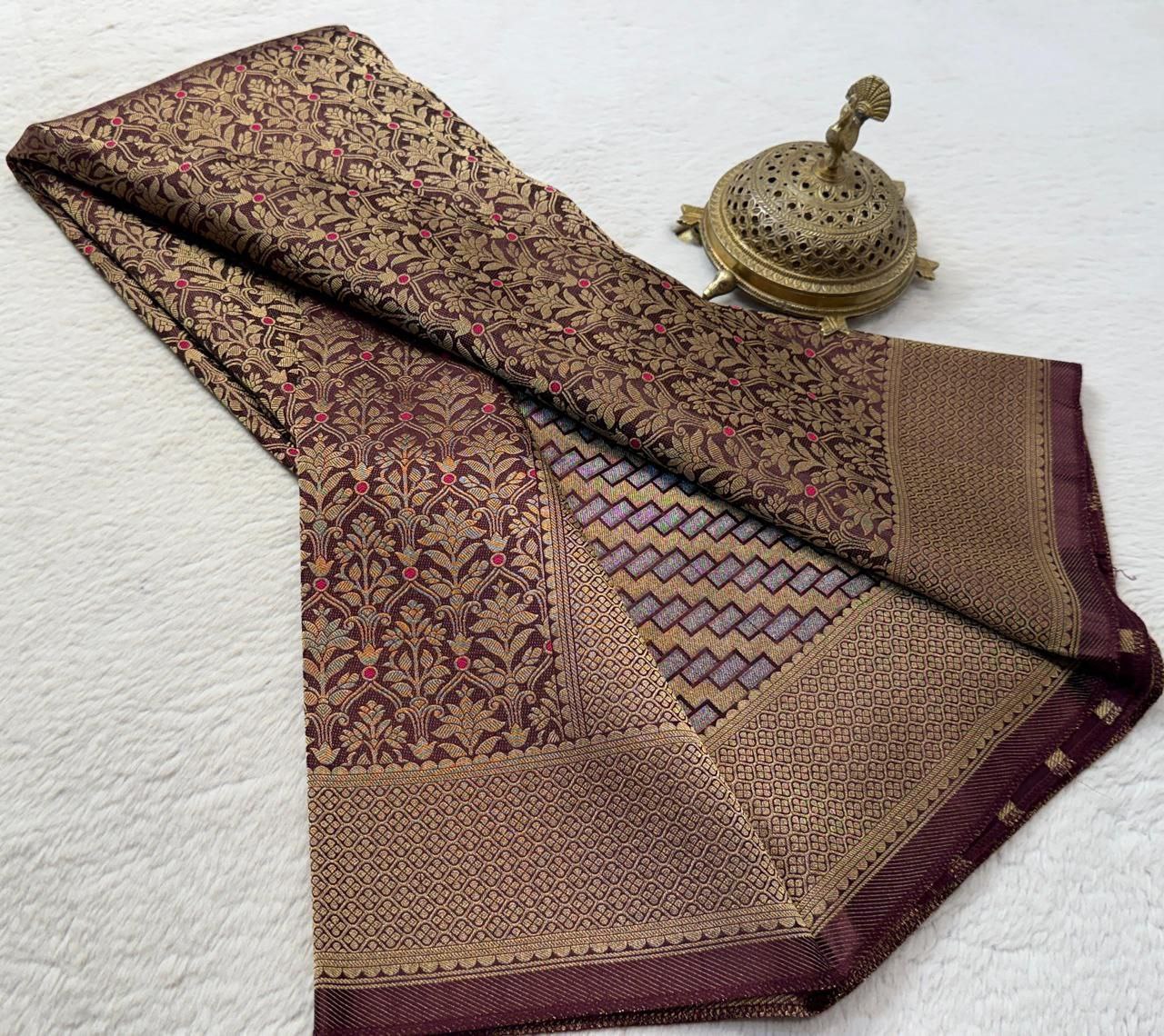 Folded brown and gold patterned fabric with a decorative metal object on a white background