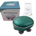 A smart scalp massager shown with its retail box, instruction manual, and charging cable on a white background. The massager itself is oval-shaped with a dark teal-green body, a silver button on top, and dark gray massage spikes on the bottom.
