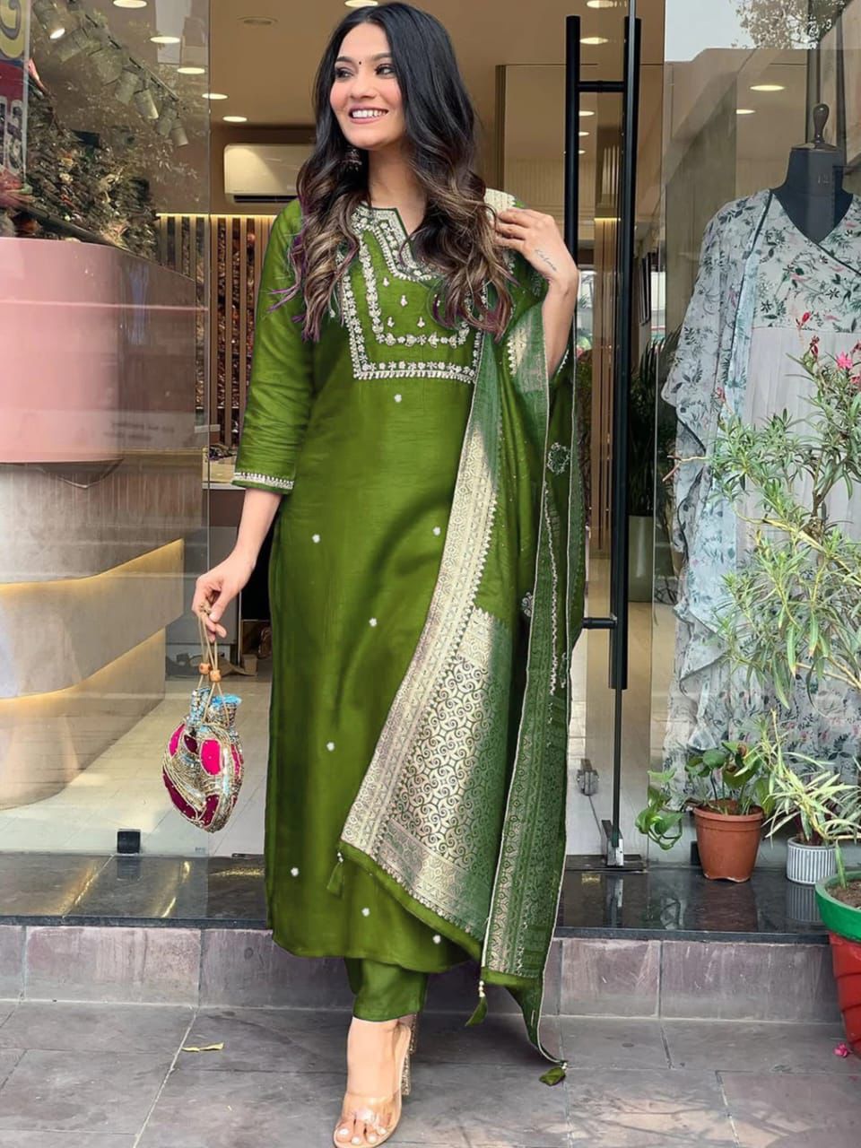 Woman in a green traditional outfit standing in front of a store entrance.