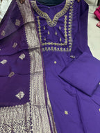 A purple traditional Indian salwar kameez suit set with gold embroidery and a matching sheer dupatta, laid out on a light floor.
