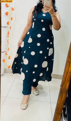 A woman takes a mirror selfie wearing a sleeveless dark teal blue A-line kurta with large white polka dots, paired with matching teal pants and beige embellished flat shoes.