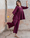 Woman in a purple outfit standing against a textured wall.