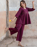 Woman in a purple outfit standing against a textured wall.