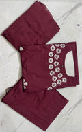 A folded three-piece women's salwar kameez set in maroon, featuring a kurta with white floral embroidery along the sleeve, paired with matching trousers and a dupatta, laid flat on a light marble surface.