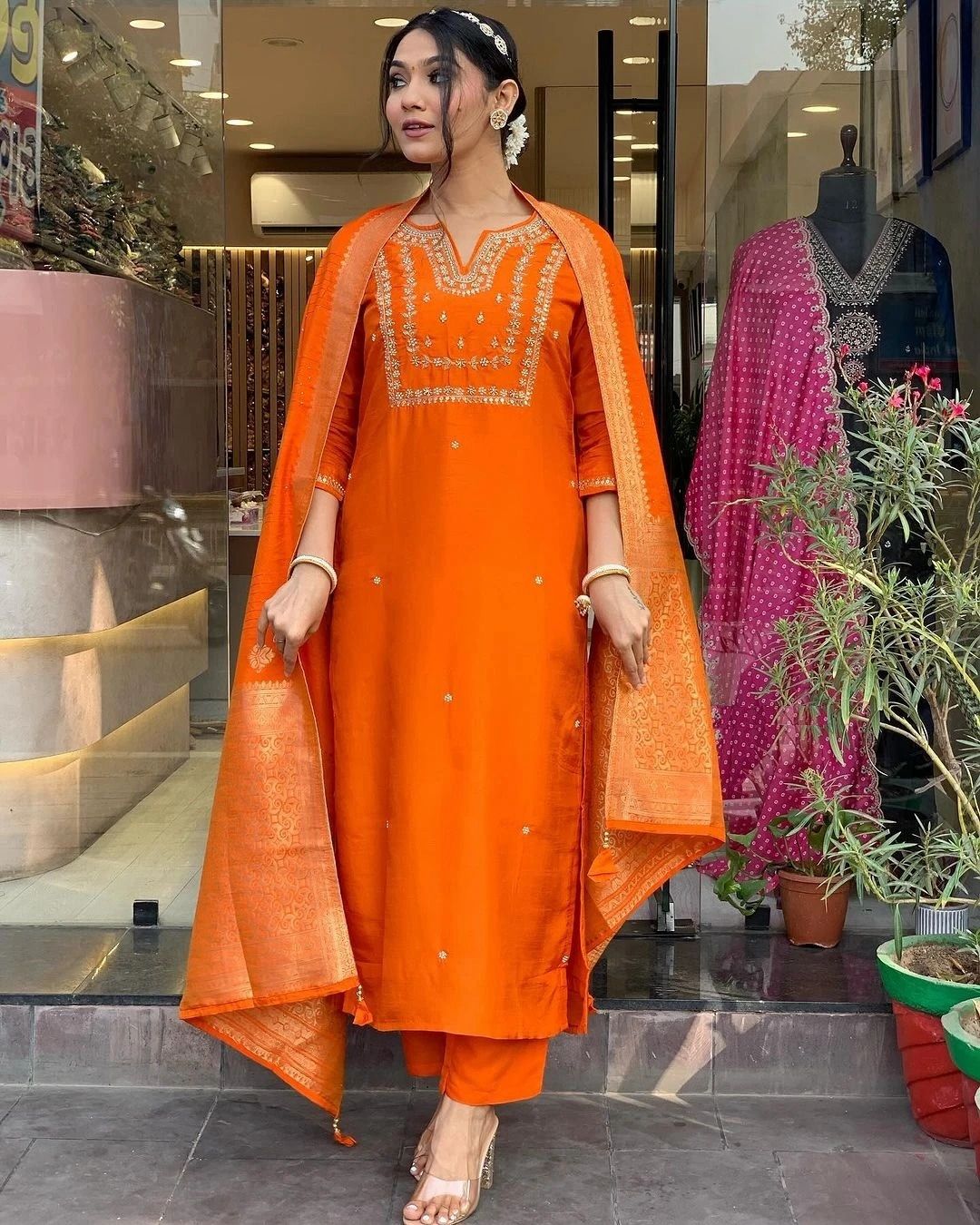 Woman in an orange traditional outfit standing in front of a store entrance.