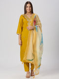 A woman modeling a mustard yellow traditional kurta set with matching pants and a sheer printed dupatta, photographed against a light gray studio background.