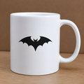 White mug with a black bat design on a wooden surface and brown background