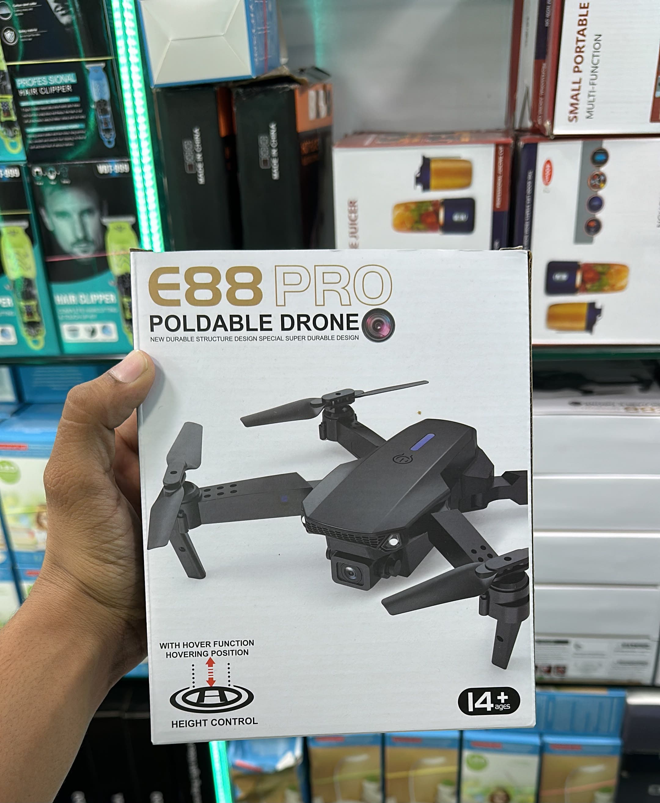 A hand holds a white box for the E88 Pro foldable drone in a retail store setting with other product boxes in the background.