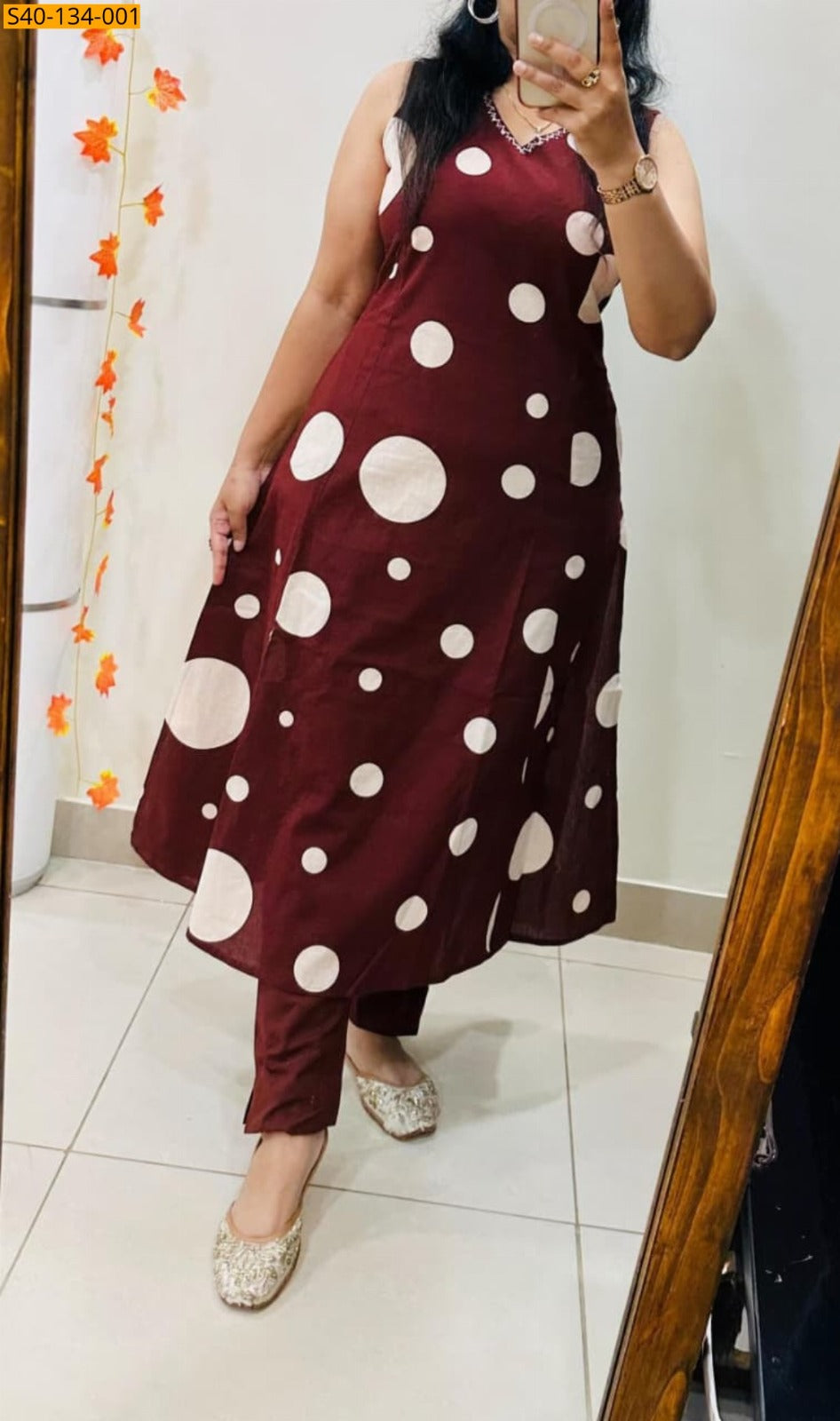 A woman takes a mirror selfie wearing a sleeveless maroon A-line kurta with large white polka dots and matching maroon trousers, paired with beige embellished flat shoes.