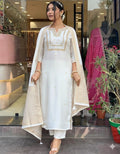 Woman in a white traditional outfit with gold embroidery standing in front of a store entrance.