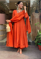 Woman in an orange traditional outfit standing in front of a store entrance.