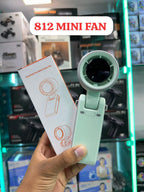 A hand holds a mint green handheld portable tube fan next to its white packaging box in a retail store setting. A white text bubble at the top reads '812 MINI FAN'.