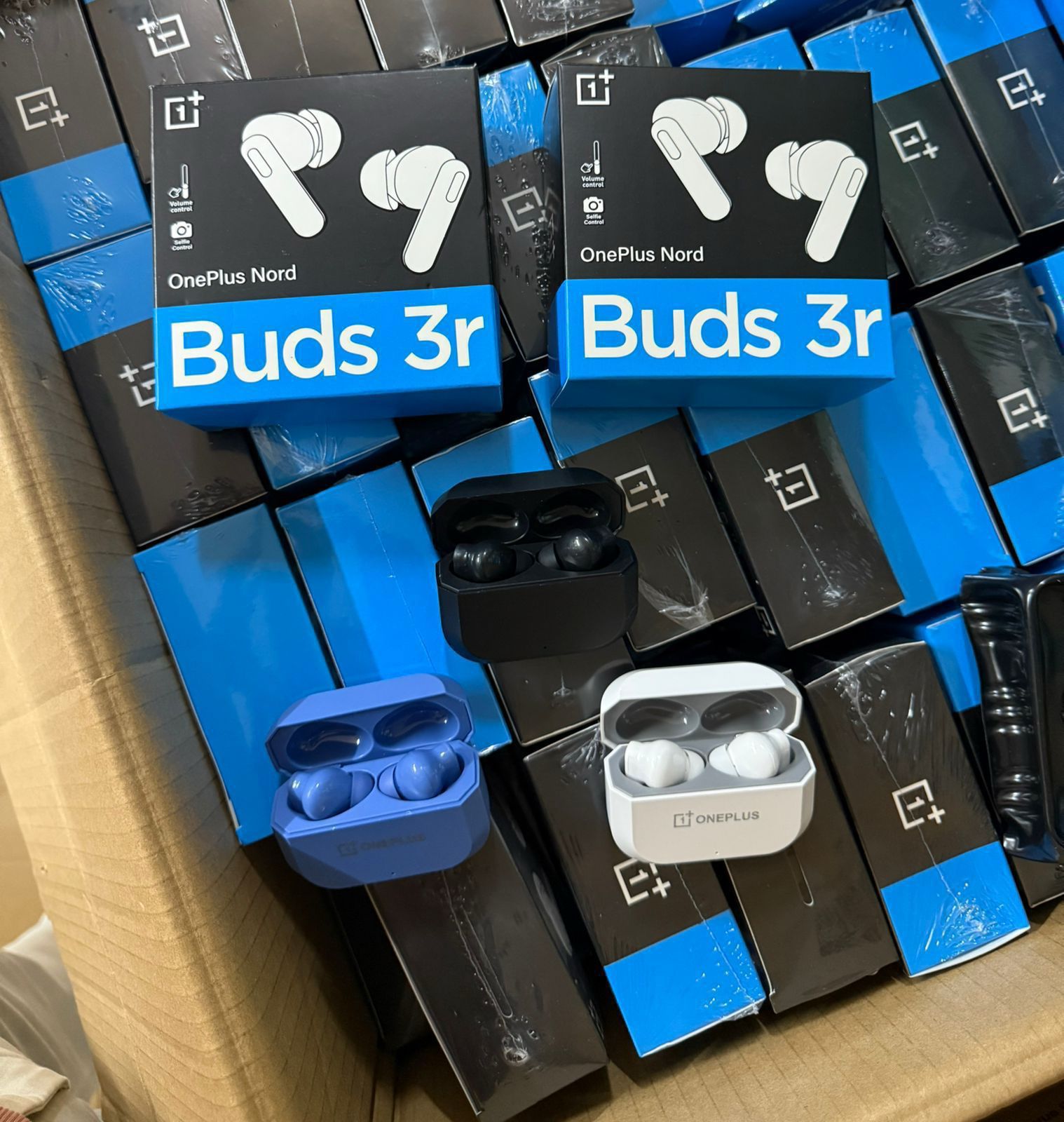 Three pairs of OnePlus Nord Buds 3r wireless earbuds in their charging cases, displayed alongside their black and blue retail packaging inside a cardboard box.