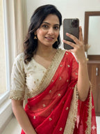 Woman taking a mirror selfie wearing a red and white saree with gold details.