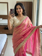 Woman in a pink saree taking a mirror selfie in a bedroom.