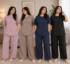 Four women modeling matching lounge sets in a softly lit living room. The sets include short-sleeve tops and wide-leg pants in dusty pink, taupe, navy blue, and black.