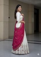 Woman in a traditional outfit with a white blouse and pink dupatta standing indoors.