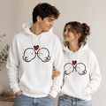 Two people wearing white hoodies with a heart and glasses design, standing close together.